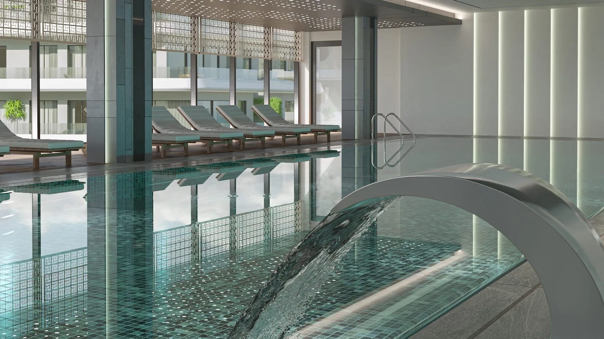 Alpcans Indoor swimming pool with lounge chairs along the side. Water cascading from a curved metallic fountain into the pool. Large windows provide natural light.